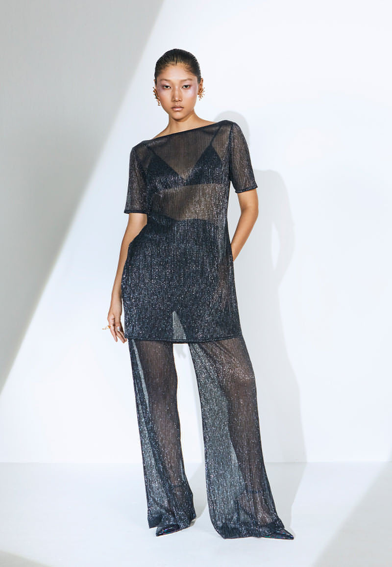 Made from pleated knit fabric, this loose-fit ensemble sets the mood for the summer. The transparent set features an airy, long top with waist-high slits on both sides. The boat neck top comes with a pair of high-waisted, straight pants with slash pockets on both sides. This lightweight blue-black knit set is an easy ready-to-wear ensemble for any party. The iridescent set comes with a black knit bralette. Finish the look with heeled sandals, sneakers or pumps and your favorite jewelry.