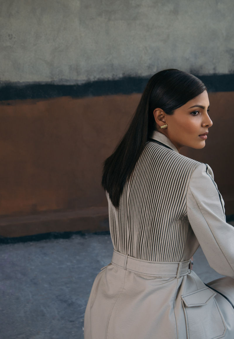 This back-pleated leather trench jacket in beige is crafted from supple rexine and lined with luxe poly-satin. This knee-length trench coat is detailed with pleating on the back, black leather piping, cargo pockets and a leather belt for fastening. Style it with a pair of pants or jeans along with boots/booties in fall and winter.