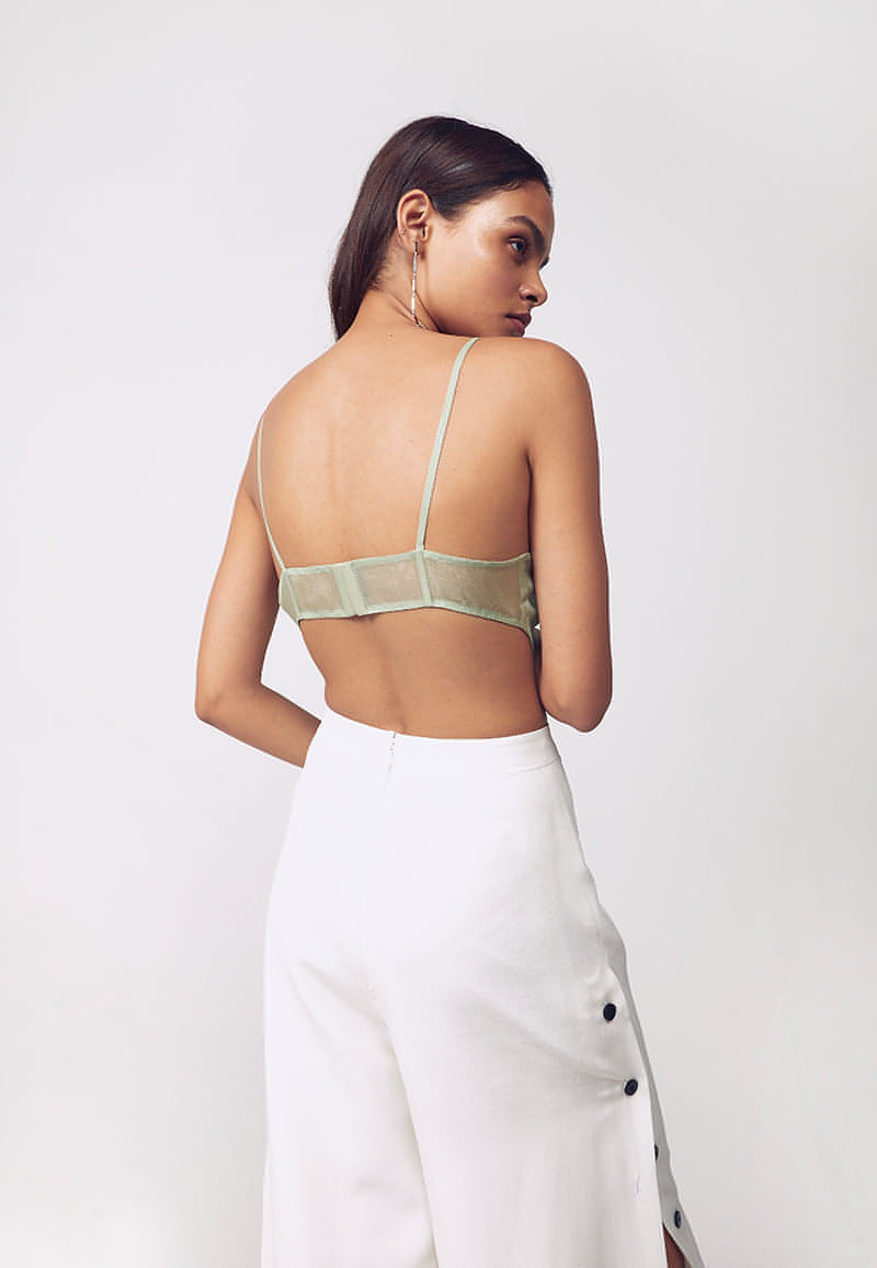 Mannat Gupta's collection of corsets, bustiers and tops. This ruched corset is made with organza in pastel green. This sleeveless, cut-out corset features ruching on the busts with a bare back. Hook and eye closures are attached at center back for seamless comfort. This minimal and versatile corsted top is perfect for any party and to deal with the summer's heat. Pair yours with one of our high-wasited pants or skirts along with heeled sandals to complete your look.  