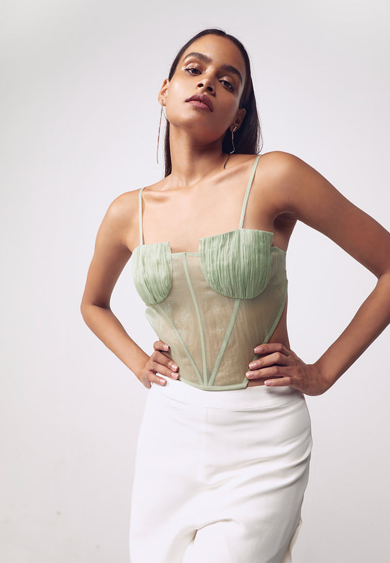 Mannat Gupta's collection of corsets, bustiers and tops. This ruched corset is made with organza in pastel green. This sleeveless, cut-out corset features ruching on the busts with a bare back. Hook and eye closures are attached at center back for seamless comfort. This minimal and versatile corsted top is perfect for any party and to deal with the summer's heat. Pair yours with one of our high-wasited pants or skirts along with heeled sandals to complete your look.  