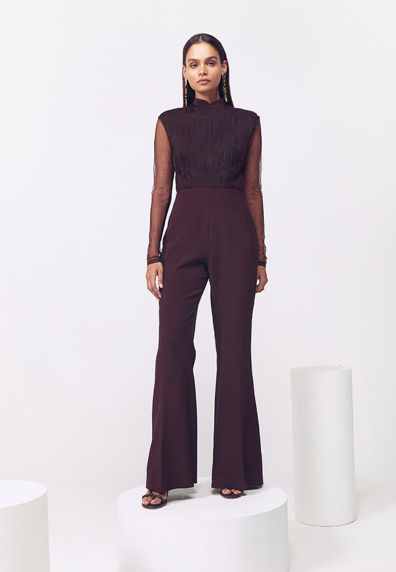 This ruched long sleeved jumpsuit with detachable peplum in wine is a curation for glam winter evenings. Crafted from luxurious silk crepe and fine net, this shoulder-padded detachable peplum jumpsuit is perfect for an evening look. This piece has a Chinese collar, minimal ruching detail on the bodice and boot-cut flared pants with a concealed zip closure at the center back. Wear the jumpsuit without the peplum for a bodycon fit and with the peplum for a comfortable one.  Style it in winters or summers